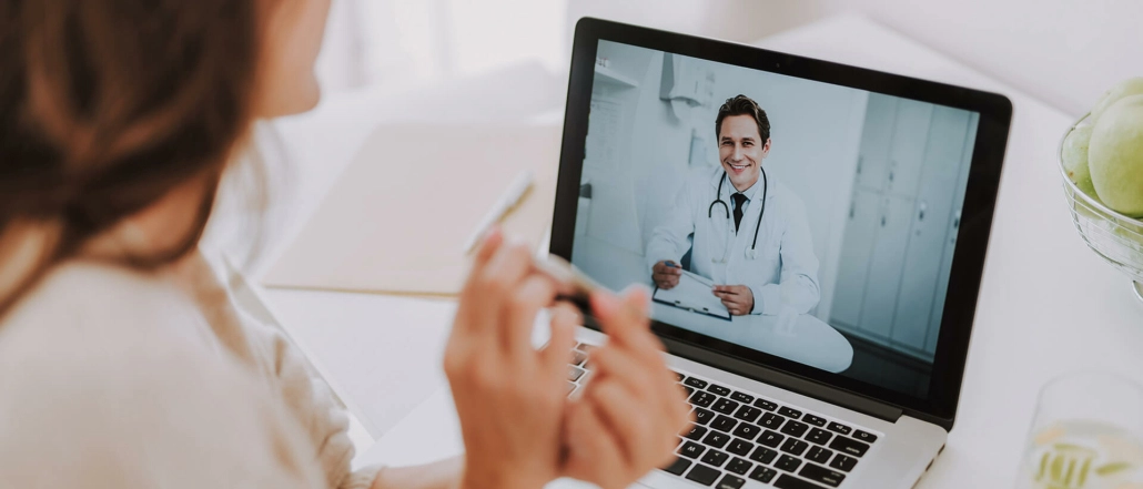 Eine Frau sitzt vor ihrem Laptop und nutzt die Telemedizin