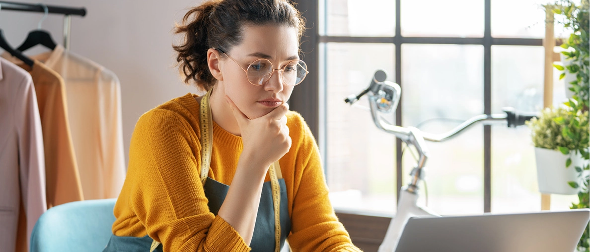 Junge Frau schaut in ihrem Atelier auf einen aufgeklappten Laptop.