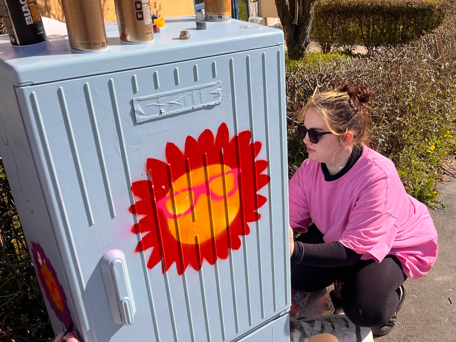 Eine Schülerin verschönert einen Stromkasten mit Graffiti. 
