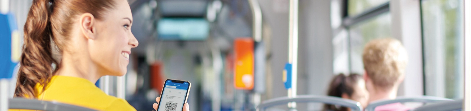 Eine Frau sitzt in der Straßenbahn. In der Hand hält sie ein Handy, auf dem ein Deutschlandticket zu sehen ist.