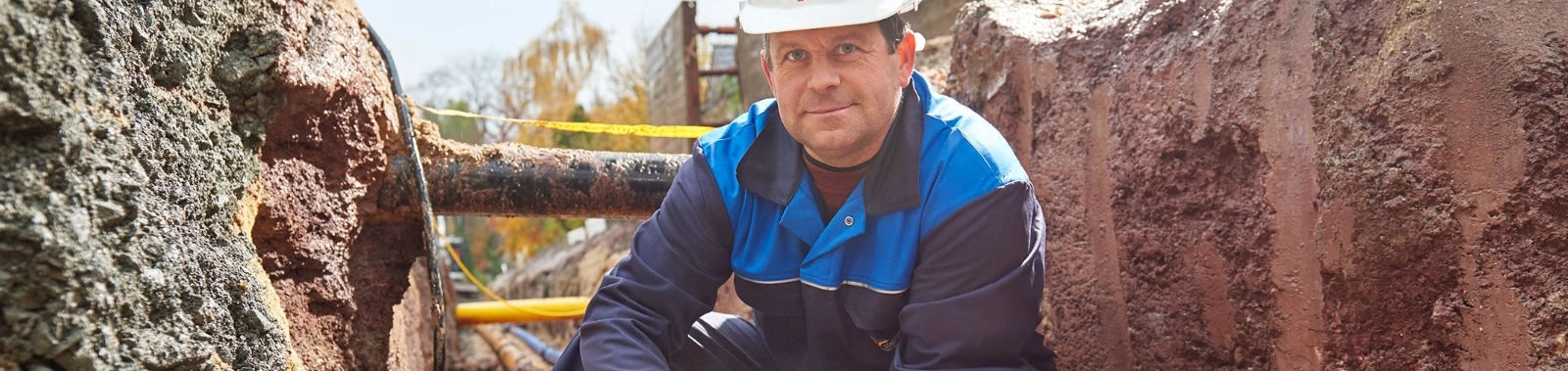 Ein Netzemitarbeitender hockt in einer Baugrube neben einem Gasrohr