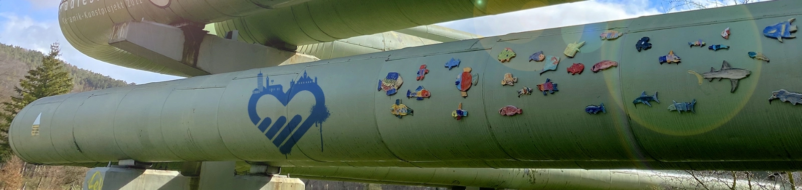 Fernwärmerohre mit bunten Verzierungen vor blauem Himmel und Sonnenschein