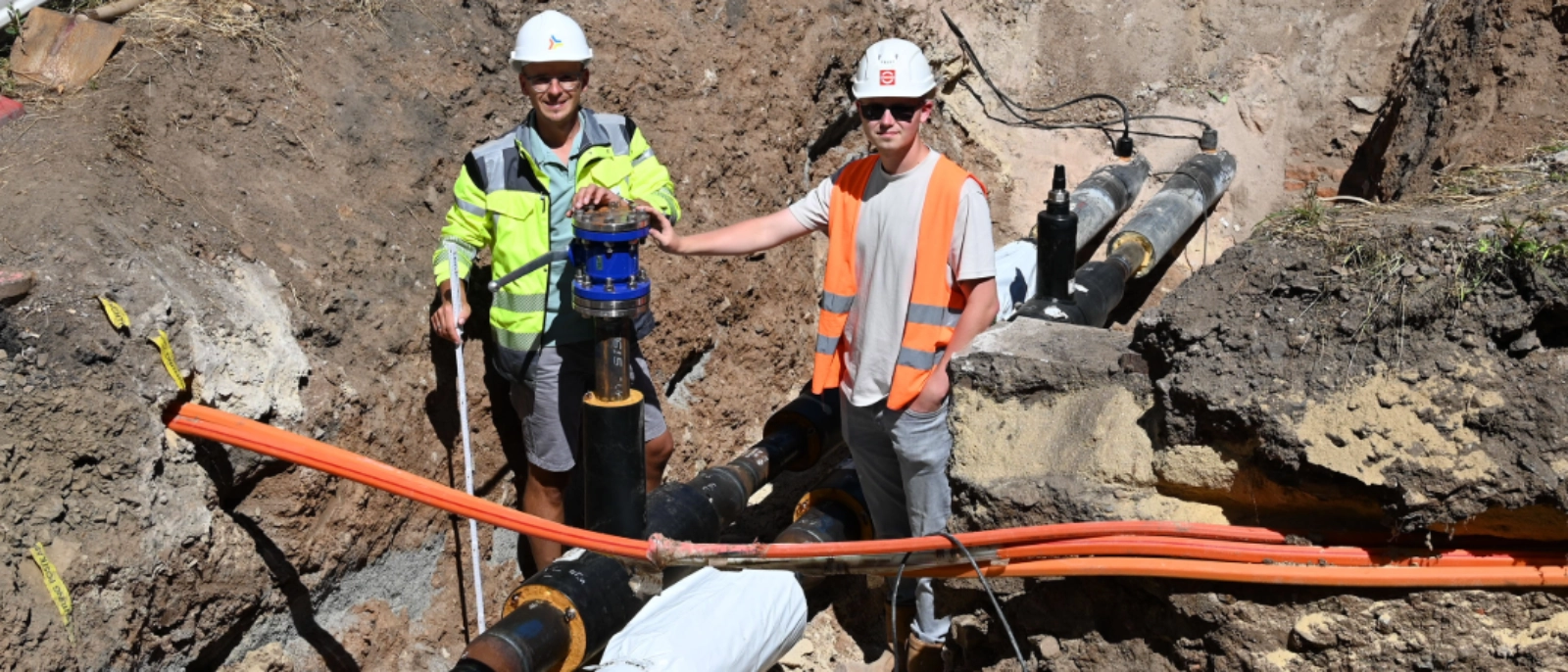 Fernwärmeausbau in Pößneck: Baugrube mit freigelegten Leitungen und zwei Arbeitenden auf der Baustelle.