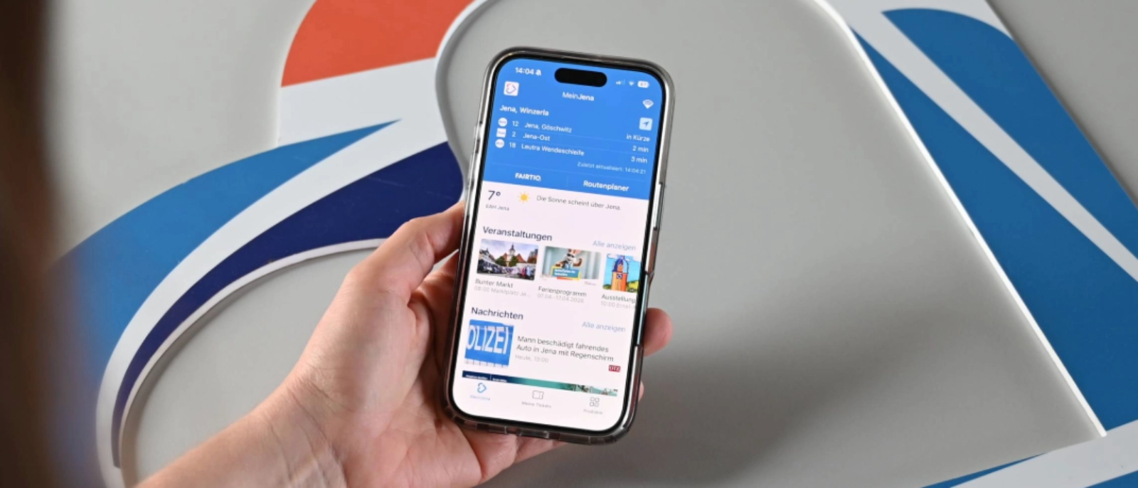 Hand hält Smartphone mit geöffneter App auf dem Bildschirm, im Hintergrund abstraktes blau-weiß-oranges Design