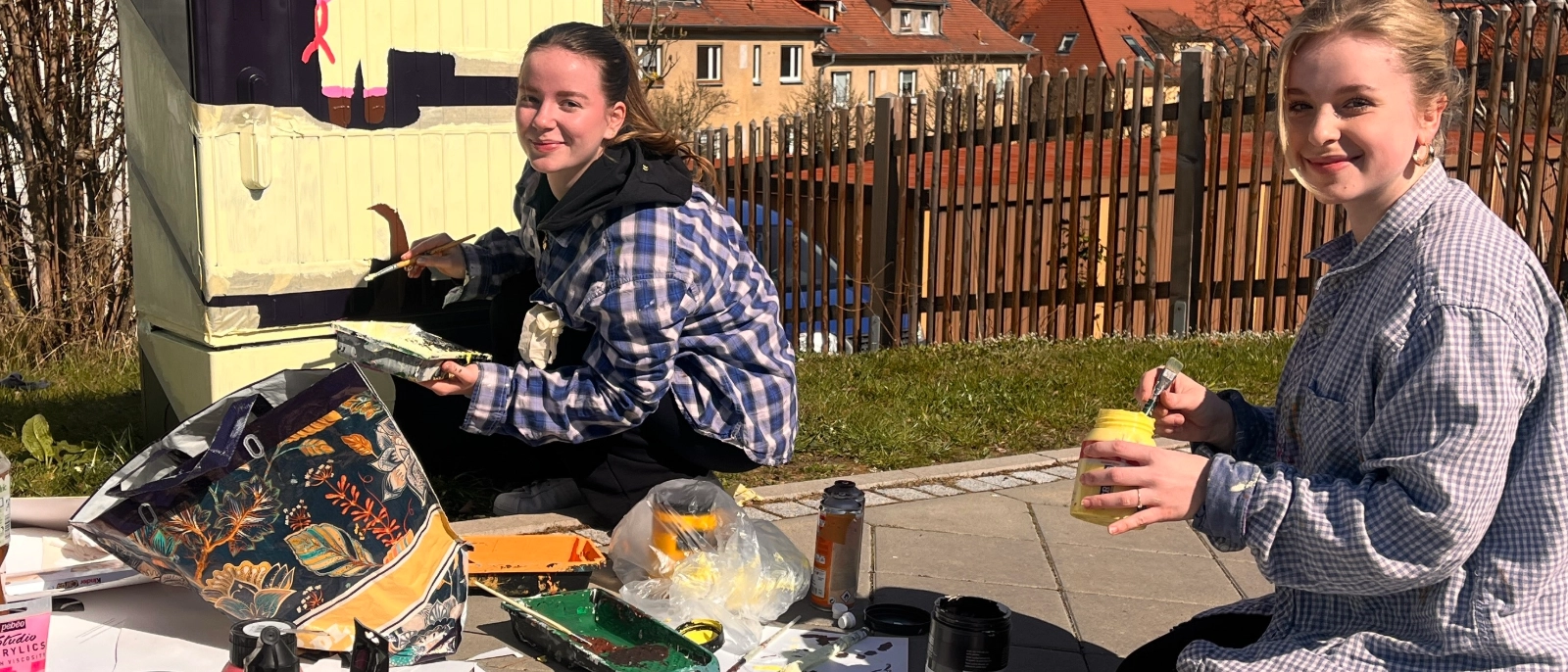 Schülerinnen verschönern einen Stromkasten mit Graffiti. 