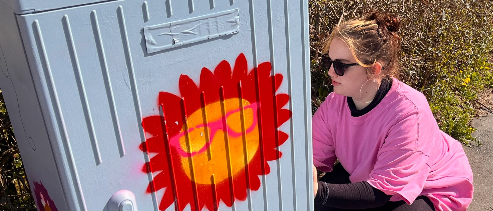 Eine Schülerin verschönert einen Stromkasten mit Graffiti. 
