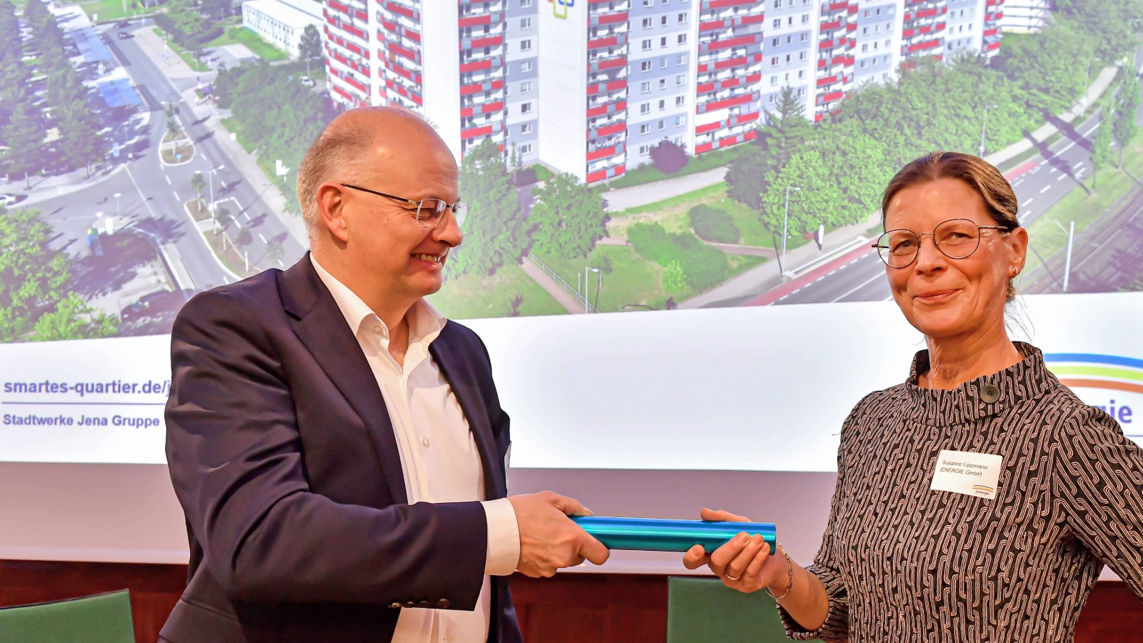 Symbolischer Staffelstabsübergang zum Projektabschluss: Der ehemalige jenergie-Geschäftsführer Tobias Wolfrum übergibt bei der Abschlussveranstaltung des Smarten Quartiers Jena-Lobeda die Verantwortung für die Weiterentwicklung der Themen an die neue Geschäftsführerin Susanne Lippmann.  