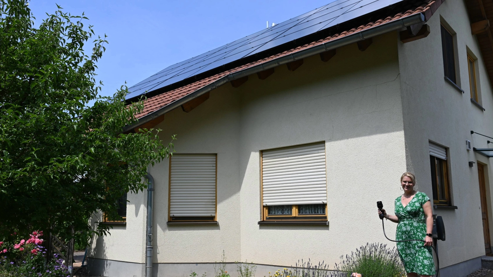 Elektromobilitäts-Expertin Djamila Neutert vor Familie Schults Haus mit PV-Anlage und Ladesäulenanschluss