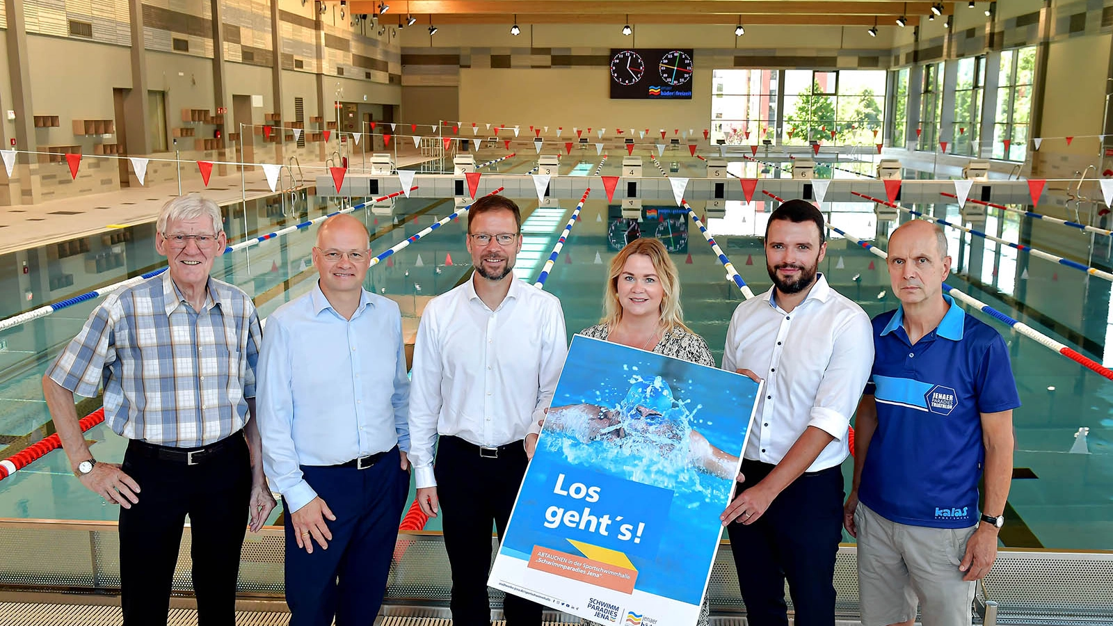 Sechs Personen stehen mit einem Plakat in der Sportschwimmhalle