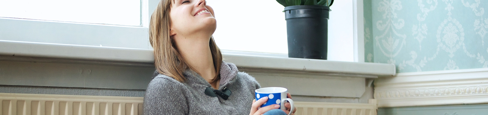 Eine Frau sitzt mit einer Kaffeetasse in der Hand an einer Heizung