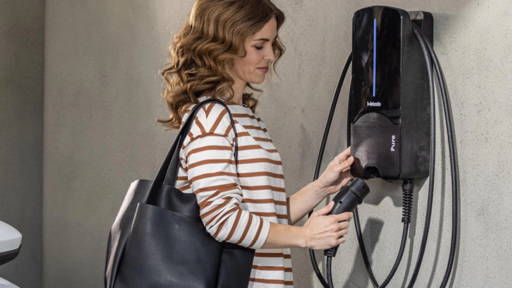 Eine Frau steht an einer Wallbox und hat den Ladestecker in der Hand