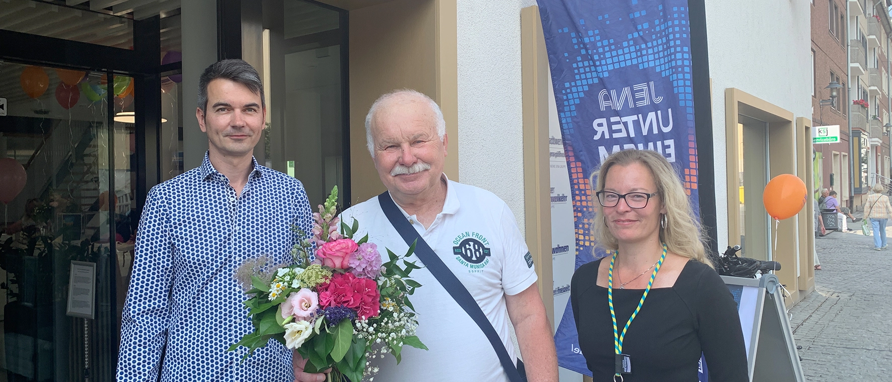 Drei Personen stehen anlässlich der einjährigen Jubiläumsfeier vor dem Kundencenter