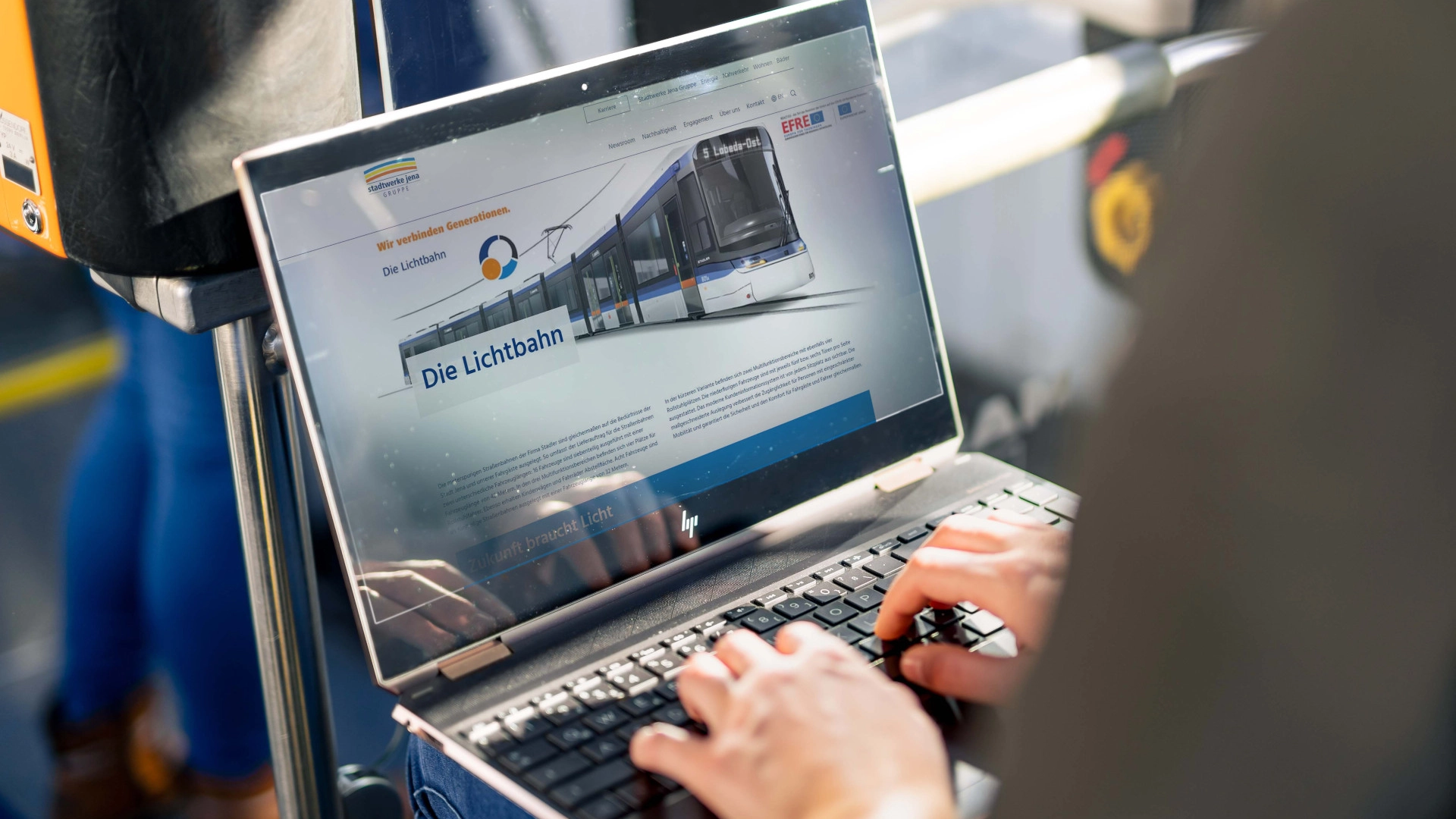 Person sitzt mit Laptop in Fahrzeug. Auf dem Laptop ist eine Website zur Lichtbahn zu sehen.