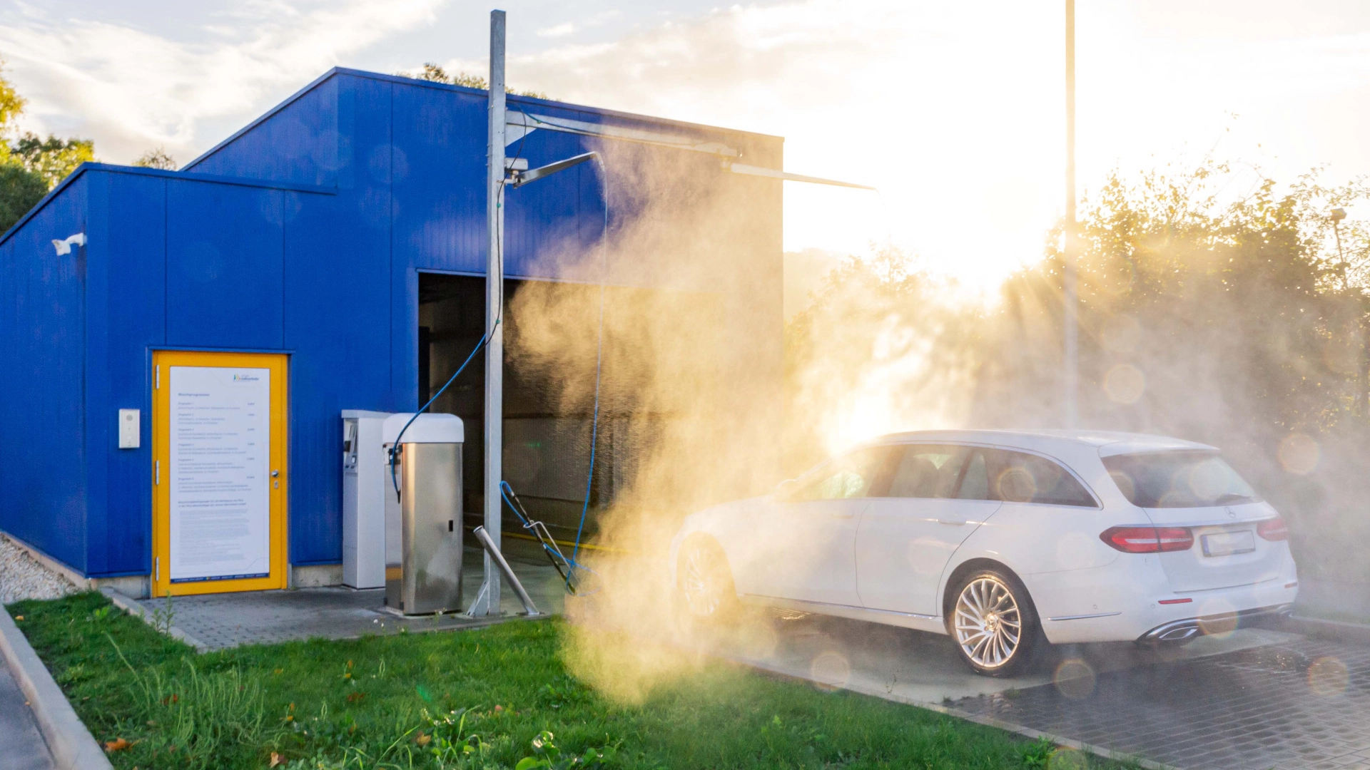 Ein Auto steht vor der Waschanlage und wird mit Wasser vorbehandelt.