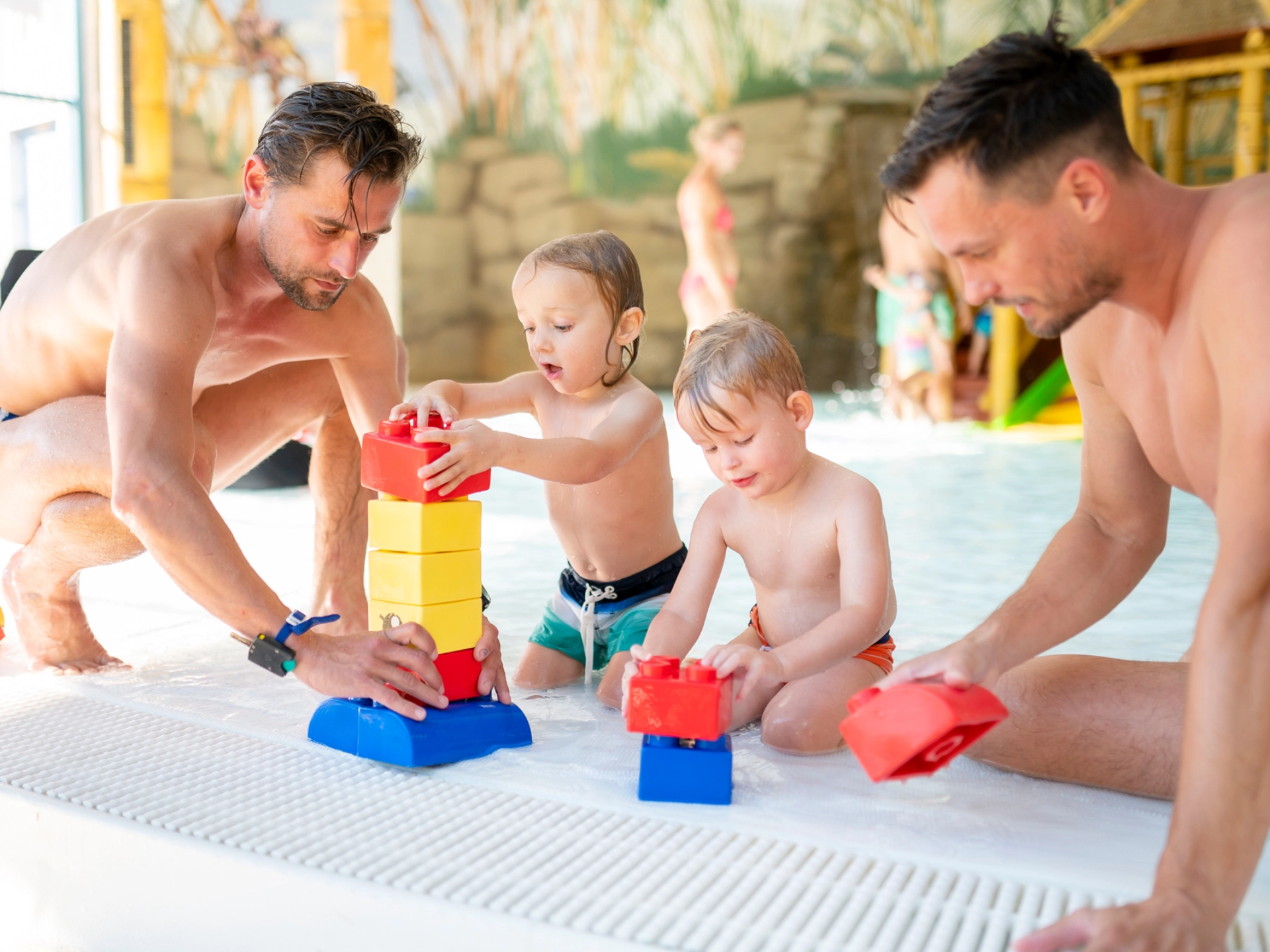 Zwei Männer und zwei Kinder spielen mit Wasserspielzeug