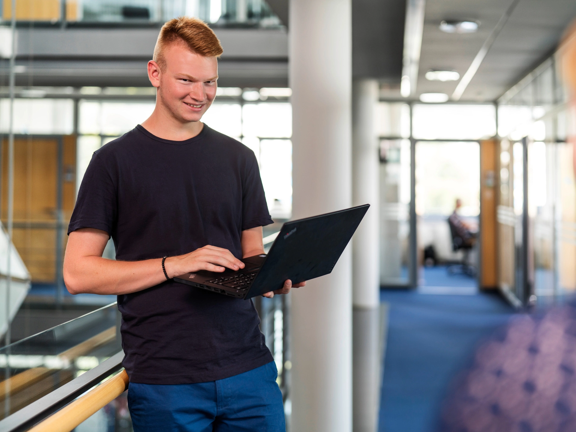 Ein junger Mann steht mit einem Laptop im Atrium. 