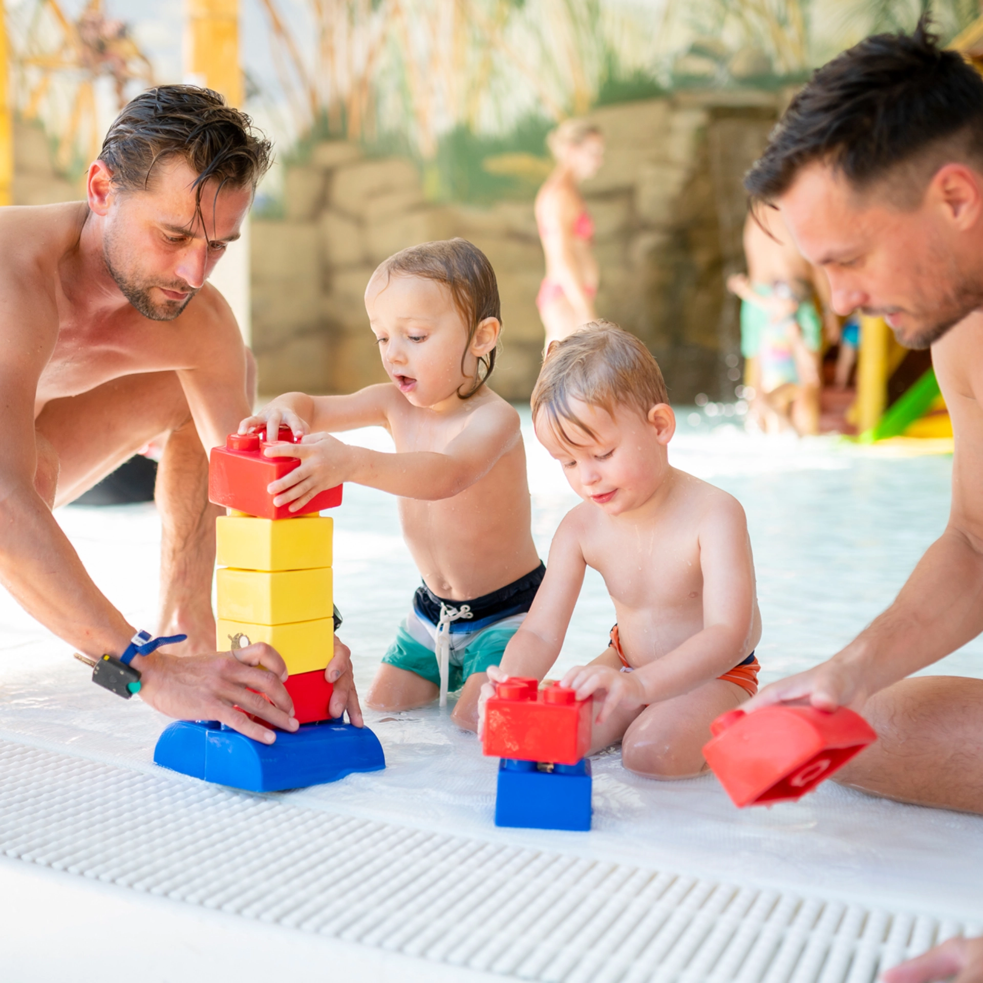 Zwei Männer und zwei Kinder spielen mit Wasserspielzeug