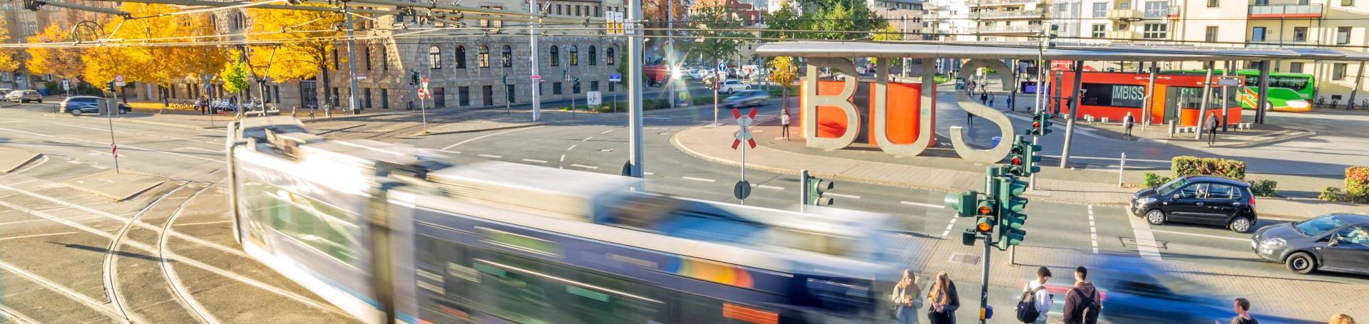 Der Busbahnhof in Jena mit einer fahrenden Straßenbahn im Vordergrund. Im Hintergrund das Volksbad.