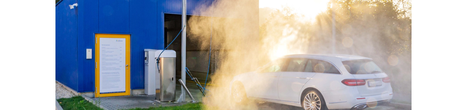 Ein Auto steht vor der Waschanlage und wird mit Wasser vorbehandelt.