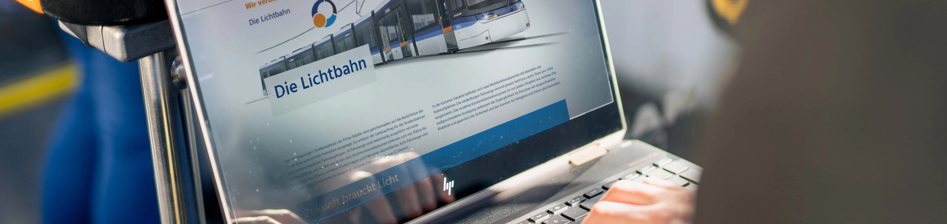 Person sitzt mit Laptop in Fahrzeug. Auf dem Laptop ist eine Website zur Lichtbahn zu sehen.