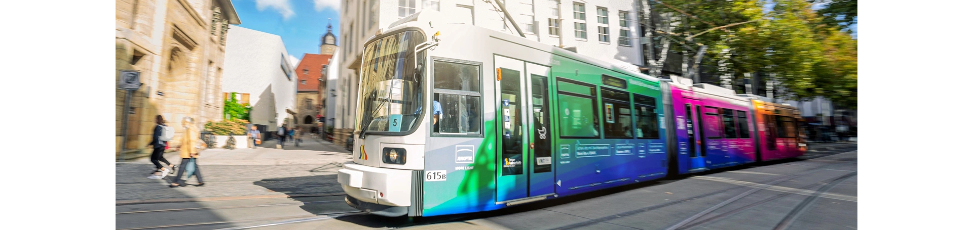 Straßenbahn fährt durch die Straßen von Jena mit Außenwerbung.