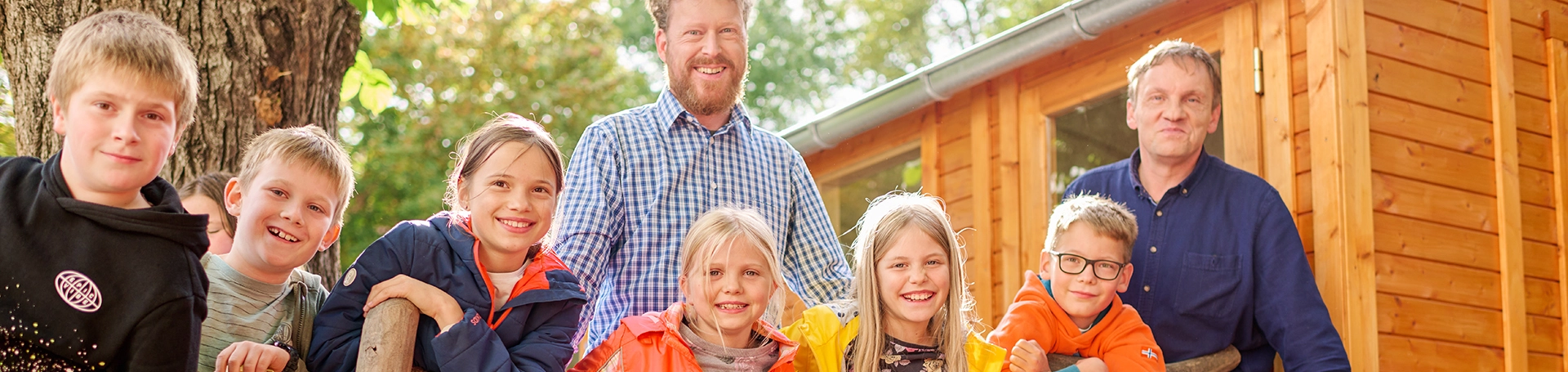 Eine Kindergruppe und zwei Erwachsene stehen vor einer Holzhütte
