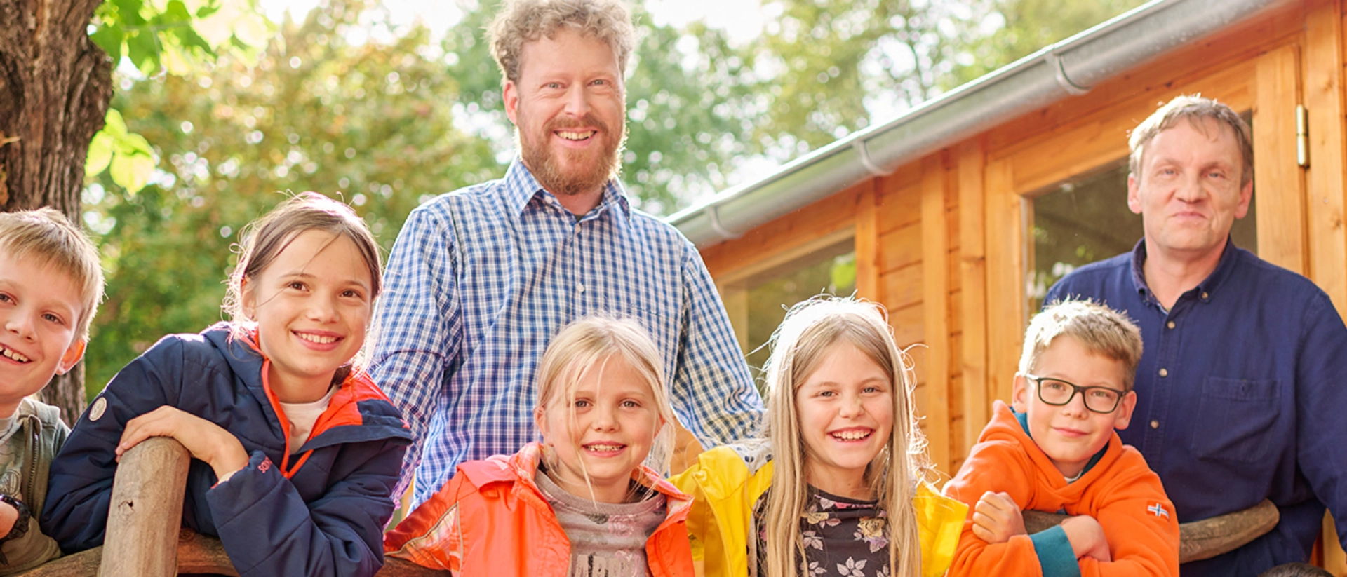 Eine Kindergruppe und zwei Erwachsene stehen vor einer Holzhütte