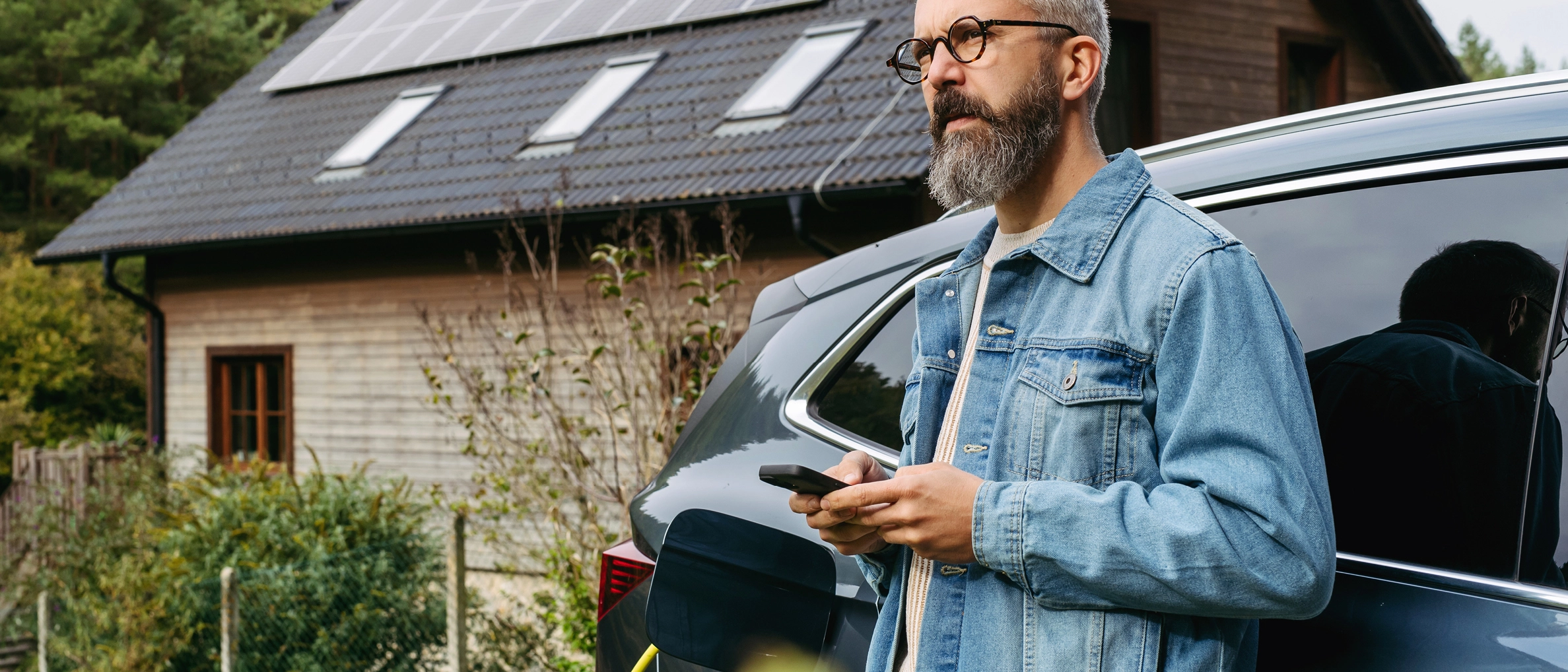 Mann lehnt an E-Auto, welches gerade geladen wird.