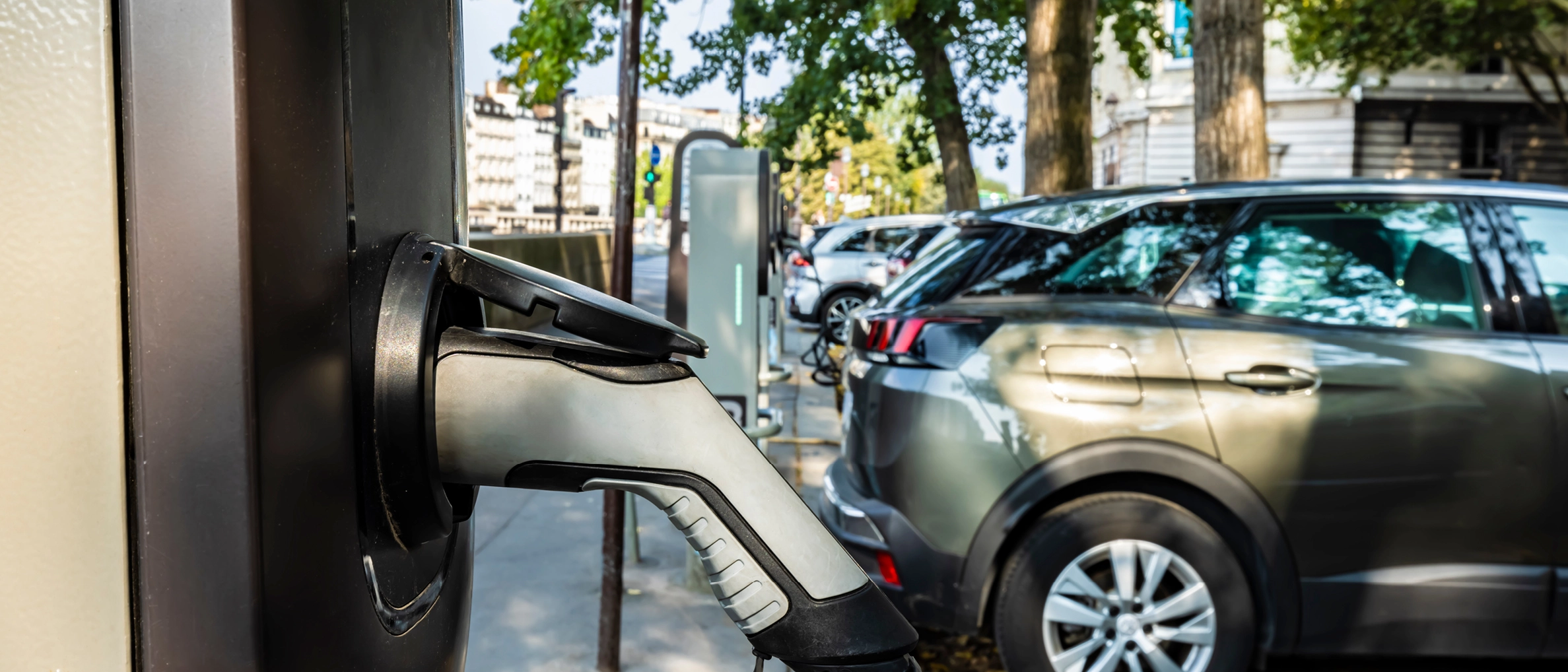 Öffentliche Ladesäule mit Ladepistole und Fahrzeugen im Hintergrund