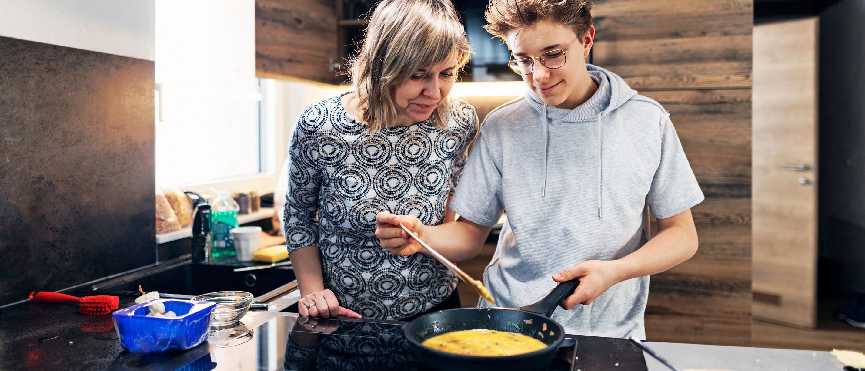 Mutter und Sohn stehen am Herd und kochen gemeinsam.