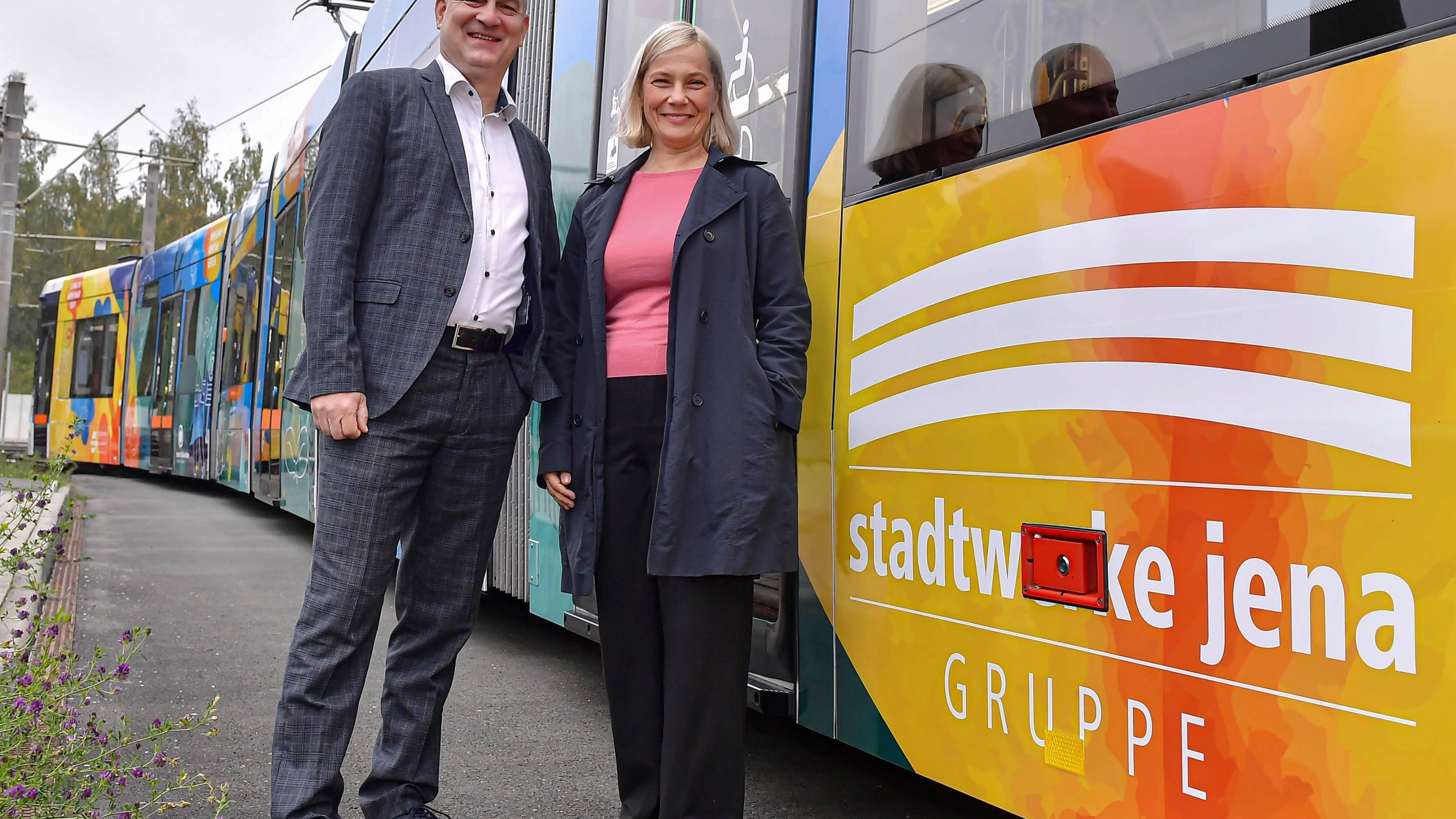 (©Stadtwerke Jena, Jürgen Scheere): Claudia Budich, Geschäftsführerin Stadtwerke Jena, und Andreas Möller, Geschäftsführer Jenaer Nahverkehr, präsentieren die neu gestaltete Straßenbahn mit der Wagennummer 802 auf dem Betriebshof des Jenaer Nahverkehrs. 