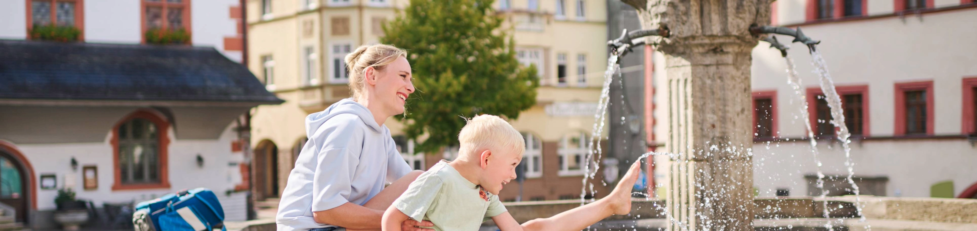Frau und Kind sitzen am Brunnen auf dem Marktplatz in Pößneck
