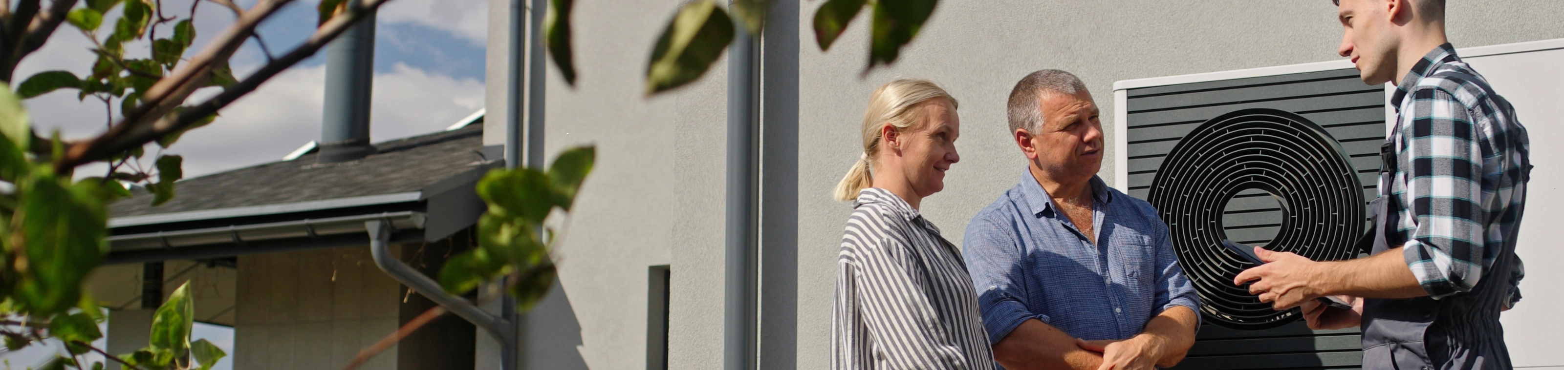 Ein Paar und ein Installateur im Gespräch vor einer Wärmepumpe