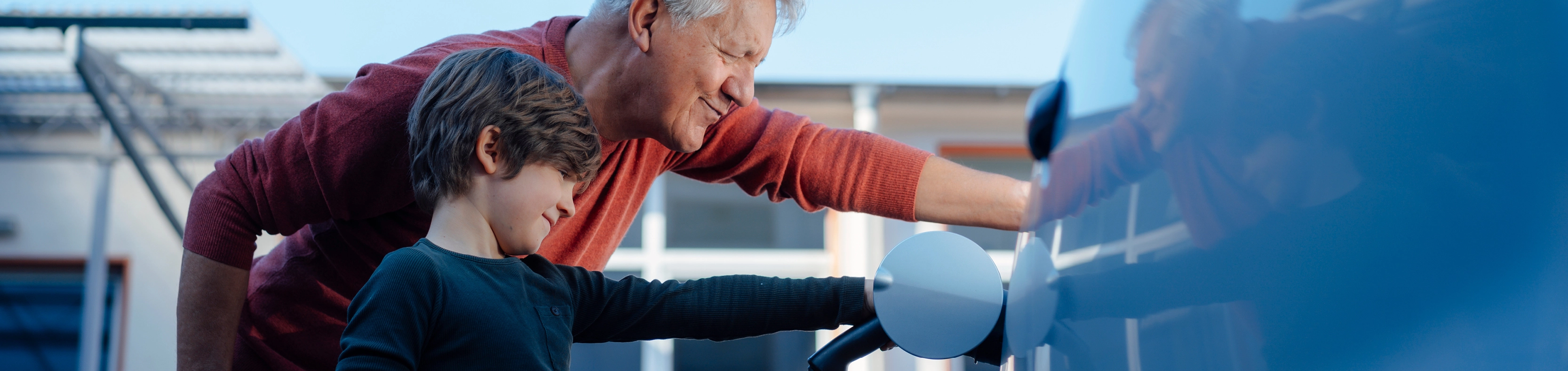 Ein Junge hält ein Ladekabel, welches ein Auto lädt und schaut mit seinem Opa beim E-Laden zu