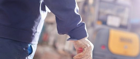 Eine Person betritt eine Baustelle und hält einen Kegel in der Hand