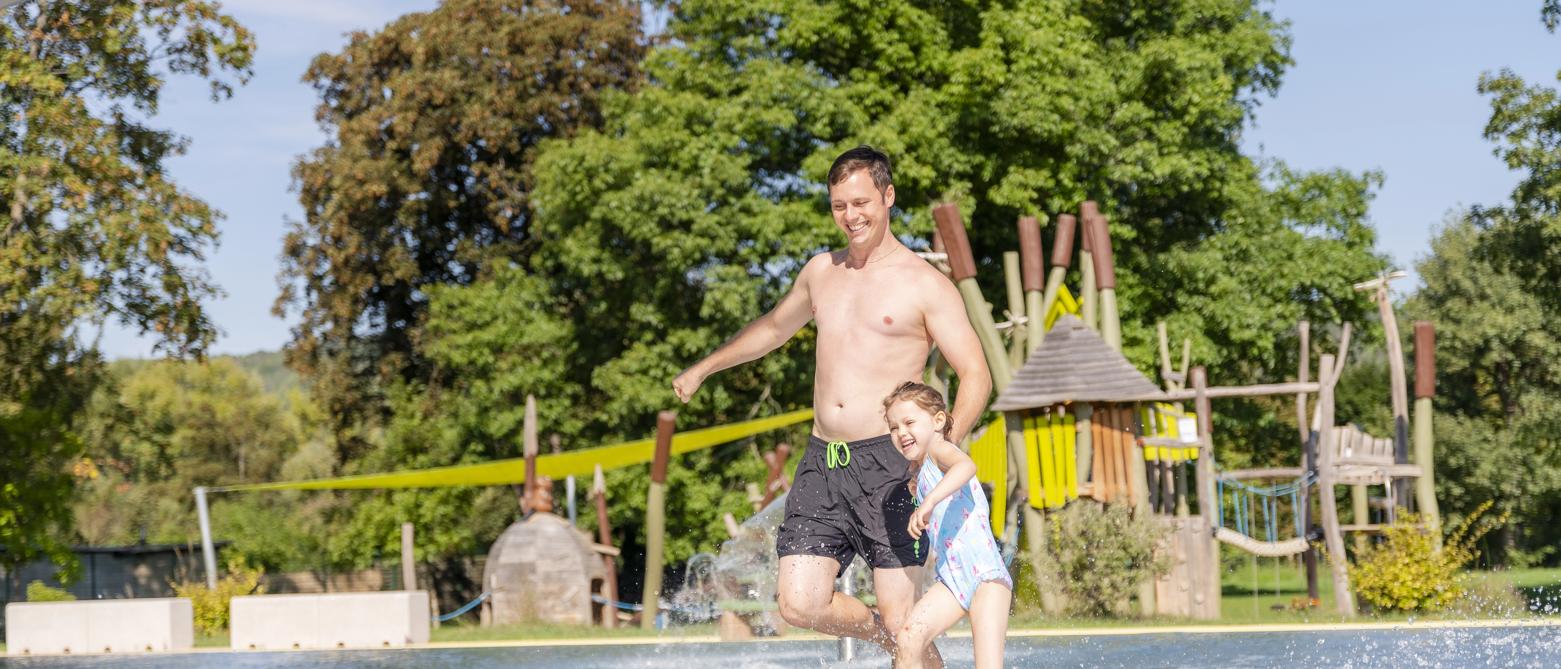 Ein Vater rennt mit seiner Tochter in ein Wasserbecken