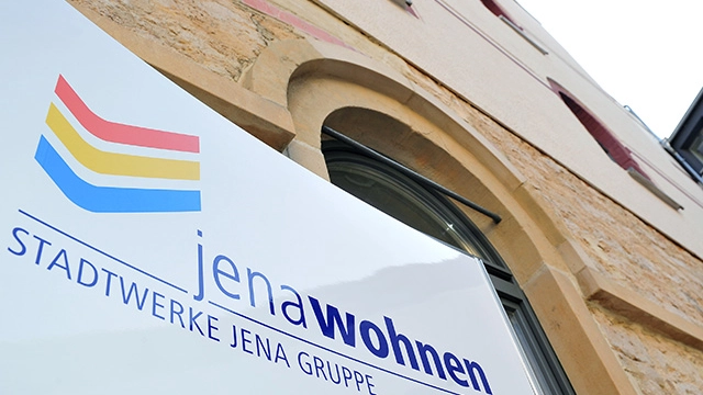 Ein jenawohnen-Schild, hängend an einer Hauswand