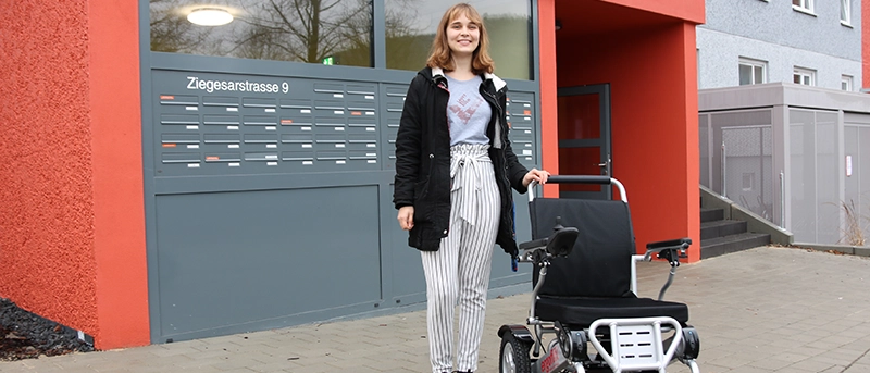 Frau steht mit einem Rollstuhl vor dem smarten Quartier