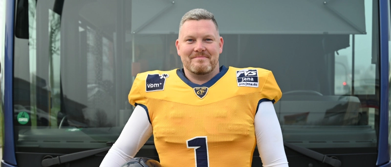 Ein Footballspieler der Hanfrieds im gelben Trikot mit Helm vor einem blauen Bus.