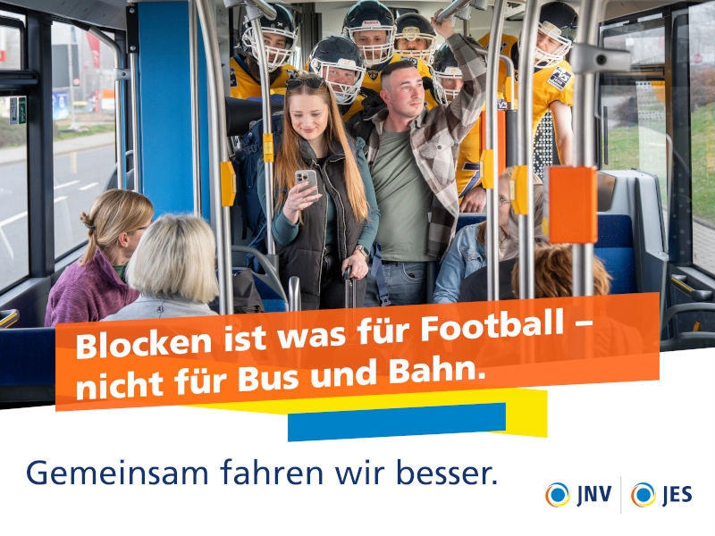 Ein Mann und eine Frau stehen im Mittelgang eines Busses, sie schaut auf ihr Handy, er aus dem Fenster. Dahinter stehen gedrängt Footballspieler, während auf den Sitzplätzen rechts und links die Fahrgäste auf das Pärchen schauen., Ein Mann und eine Frau stehen im Mittelgang eines Busses, sie schaut auf ihr Handy, er aus dem Fenster. Dahinter stehen gedrängt Footballspieler, während auf den Sitzplätzen rechts und links die Fahrgäste auf das Pärchen schauen.,