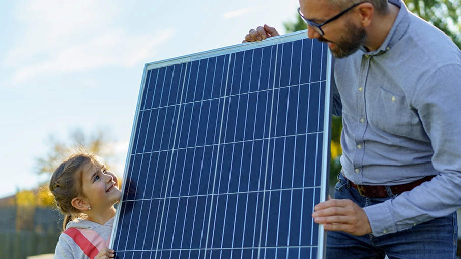 Vater und Tochter halten ein PV-Modul und schauen sich an.